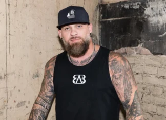 Brantley Gilbert Net Worth 2026: How the Country-Rock Firebrand Built His $18 Million Fortune Brantley Gilbert net worth hero image showing the country rock star performing live with guitar on stage in vivid red lighting.