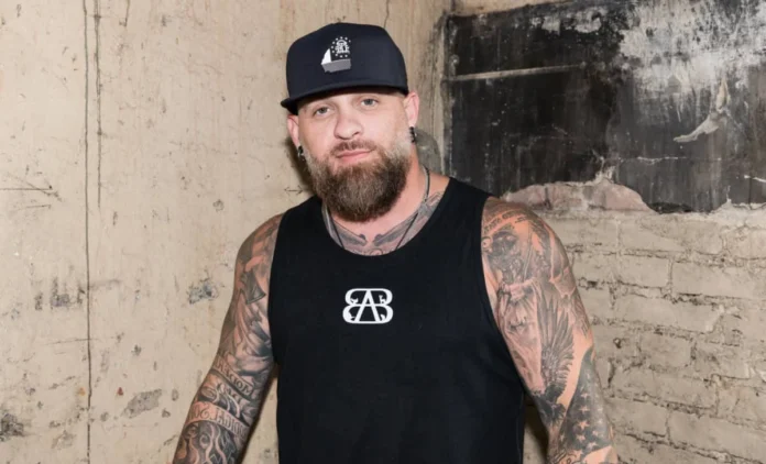 Brantley Gilbert Net Worth 2026 – Concert Performance Brantley Gilbert net worth hero image showing the country rock star performing live with guitar on stage in vivid red lighting.