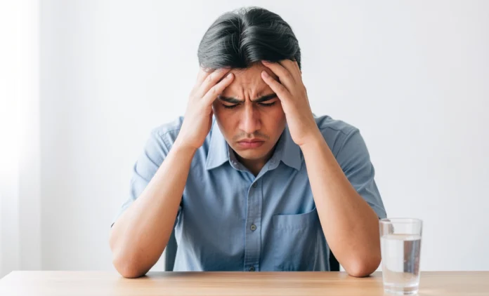 Dehydration Headache Symptoms and Relief Person holding their head in pain next to a glass of water — dehydration headache symptoms and relief