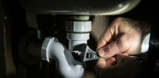 Homeowner fixing leaking pipe under sink with adjustable wrench and bucket