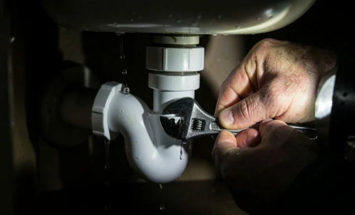 Homeowner fixing leaking pipe under sink with adjustable wrench and bucket