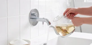 Person using boiling water and baking soda to unclog shower drain naturally in bright white bathroom
