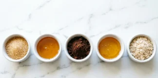Flat lay of diy body scrub recipes ingredients including sugar, coconut oil, coffee grounds, and honey on marble