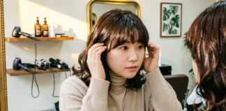 Do bangs make face look fatter — woman with round face trying curtain bangs in salon mirror
